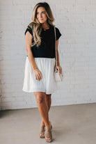 Blonde woman wearing a chic babydoll dress in black and white with a textured sweater upper, and flowy white lined skirt attached.