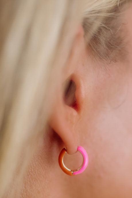 Close-up of an ear wearing a colorful hoop earring with blonde hair in the background.