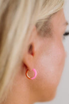 Close-up of a person wearing a gold and pink hoop earring.