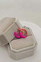 Neon pink and orange hoop earrings in a gray jewelry box on a light background