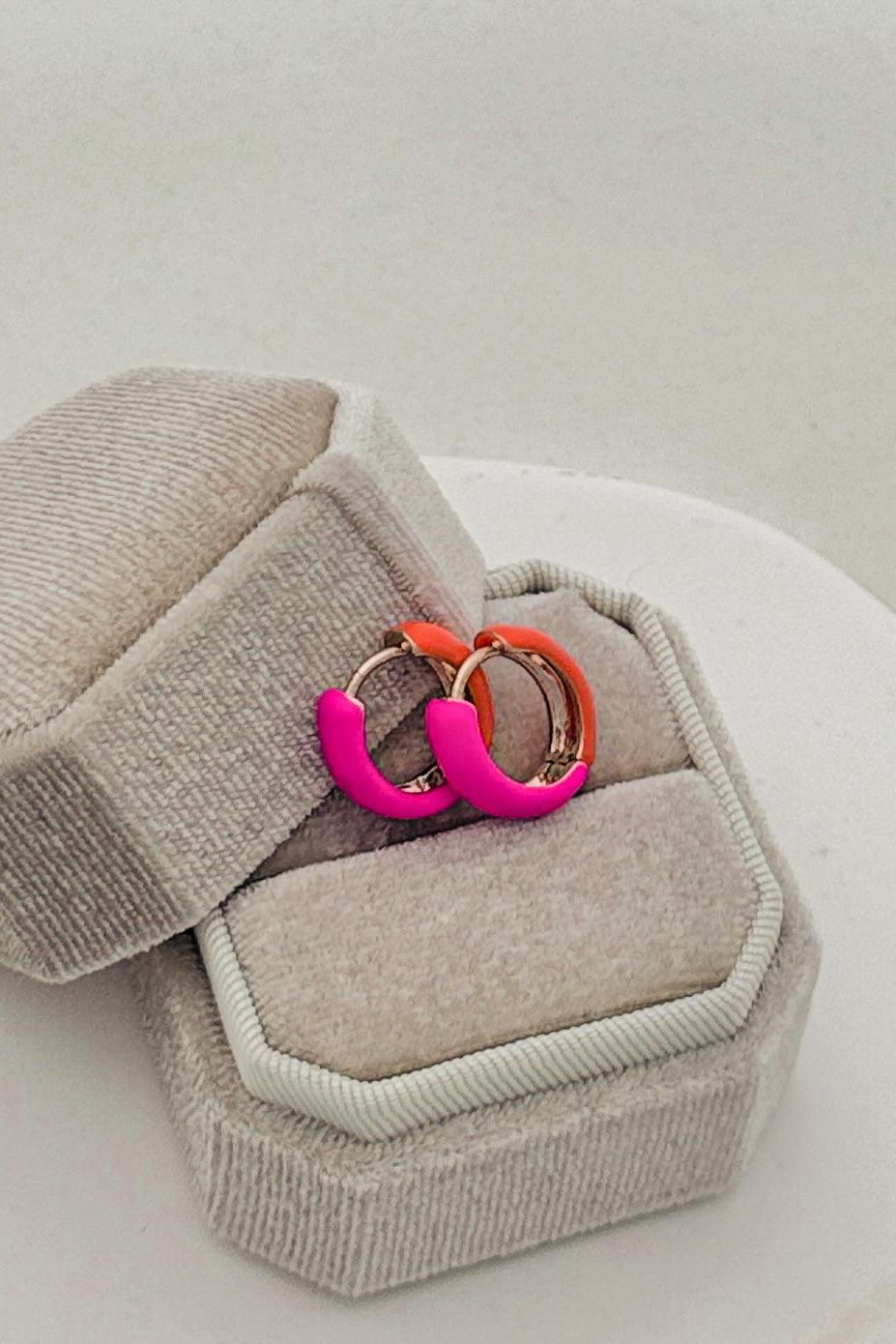 Neon pink and orange hoop earrings in a gray jewelry box on a light background