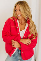 Woman wearing a red cardigan over a white shirt and blue jeans, standing against a plain background.