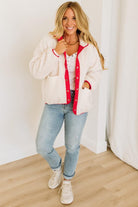 Woman wearing a white cardigan with red trim, white shirt, blue jeans, and white sneakers indoors.