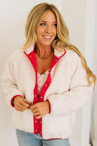 Woman wearing a white cardigan with red trim and buttons, smiling against a white background