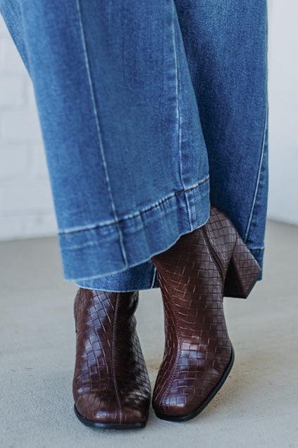 Brown crocodile-patterned boots worn with blue jeans on a light gray floor.