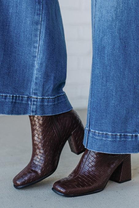 Brown crocodile-patterned boots worn with blue jeans on a light gray background
