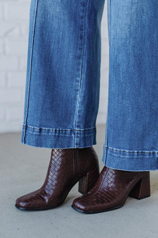 Brown woven boots worn with blue jeans on a neutral background