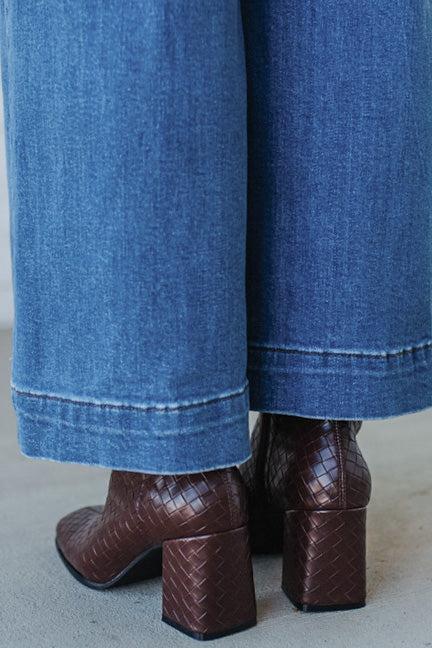 Brown woven boots with blue jeans on a neutral background