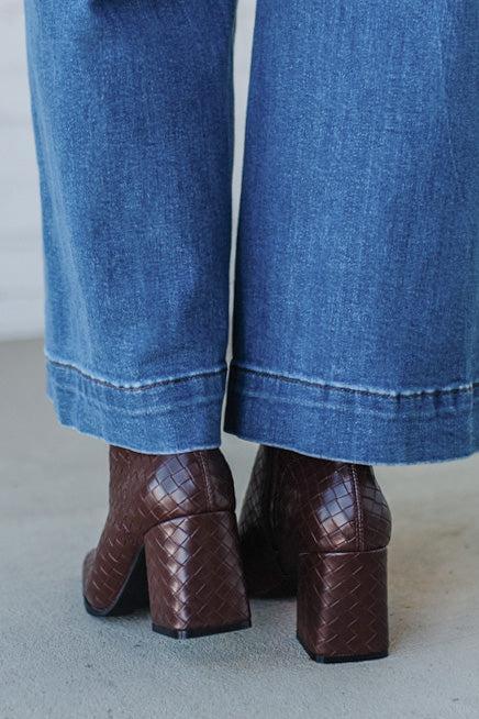 Brown woven block-heel shoes worn with blue jeans on a light gray background