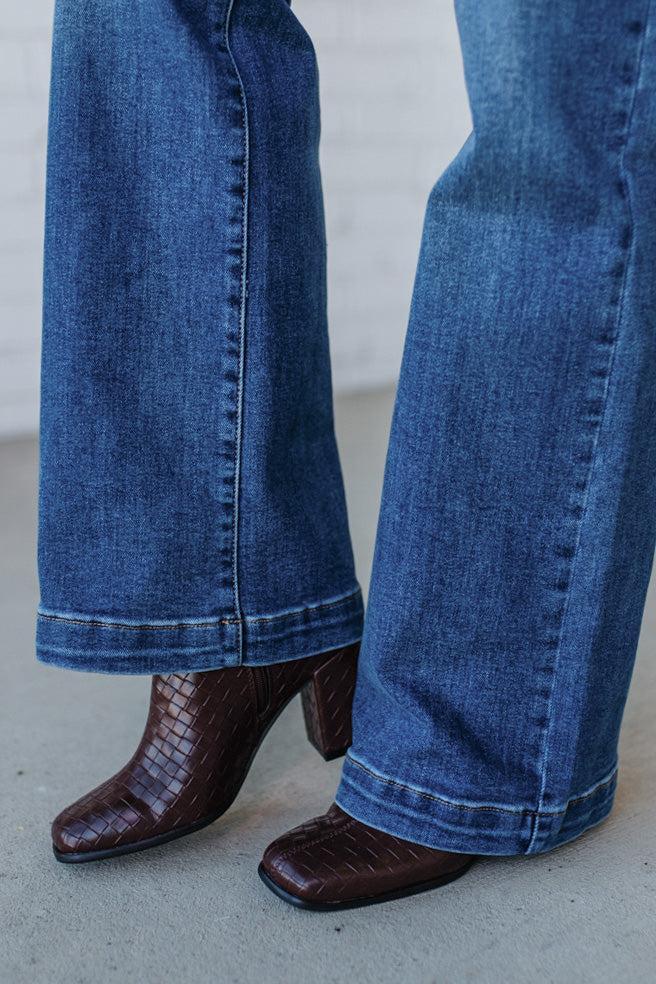 Blue jeans worn with brown crocodile-patterned high-heeled shoes on a neutral background