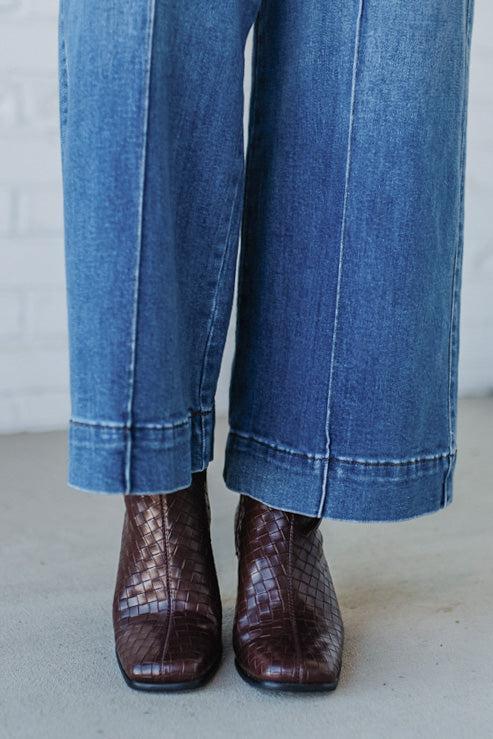 Cropped jeans worn with brown leather boots on a neutral background