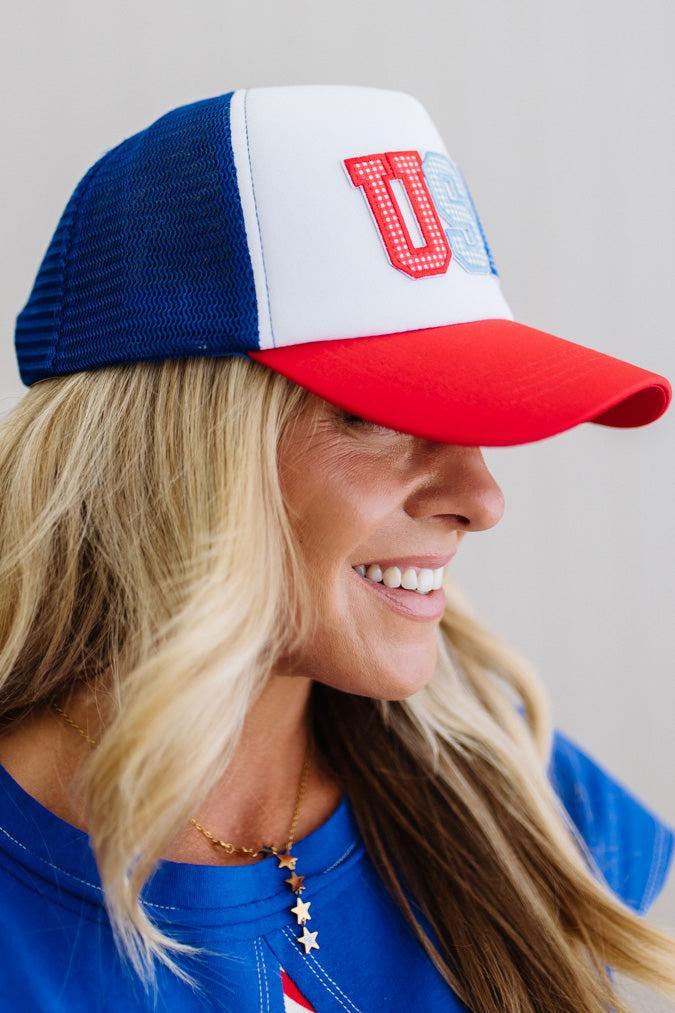 Woman wearing a blue, white, and red cap with a logo, smiling against a neutral background.