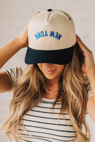 Blonde Woman wearing a Trucker Hat with Blue Upside Down embroidered: New York at the front center. Cream hat with Black Brim and accents.