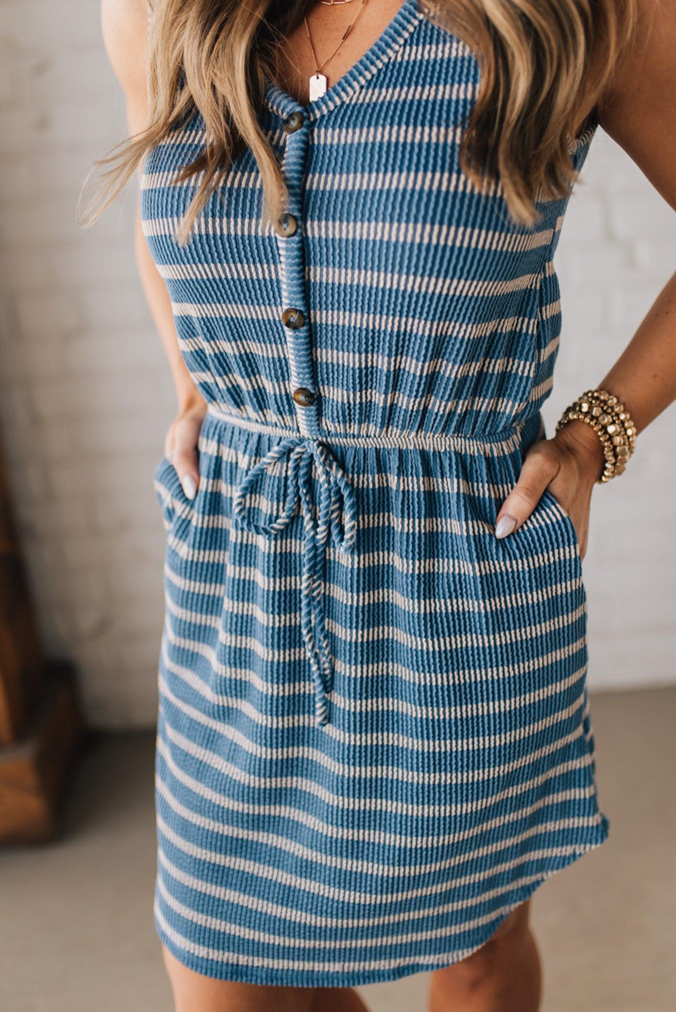 Blonde woman in a hat wearing a V-NECK, FAUX BUTTON UP, ELASTIC WAIST TIE, STRIPE DRESS WITH RIBBED TEXTURE knee length dress.