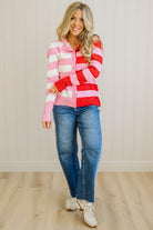 Woman wearing a pink and red striped sweater with blue jeans against a white wall.