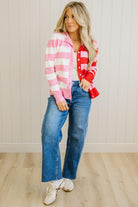 Woman wearing a red and pink plaid shirt with blue jeans against a white paneled wall.