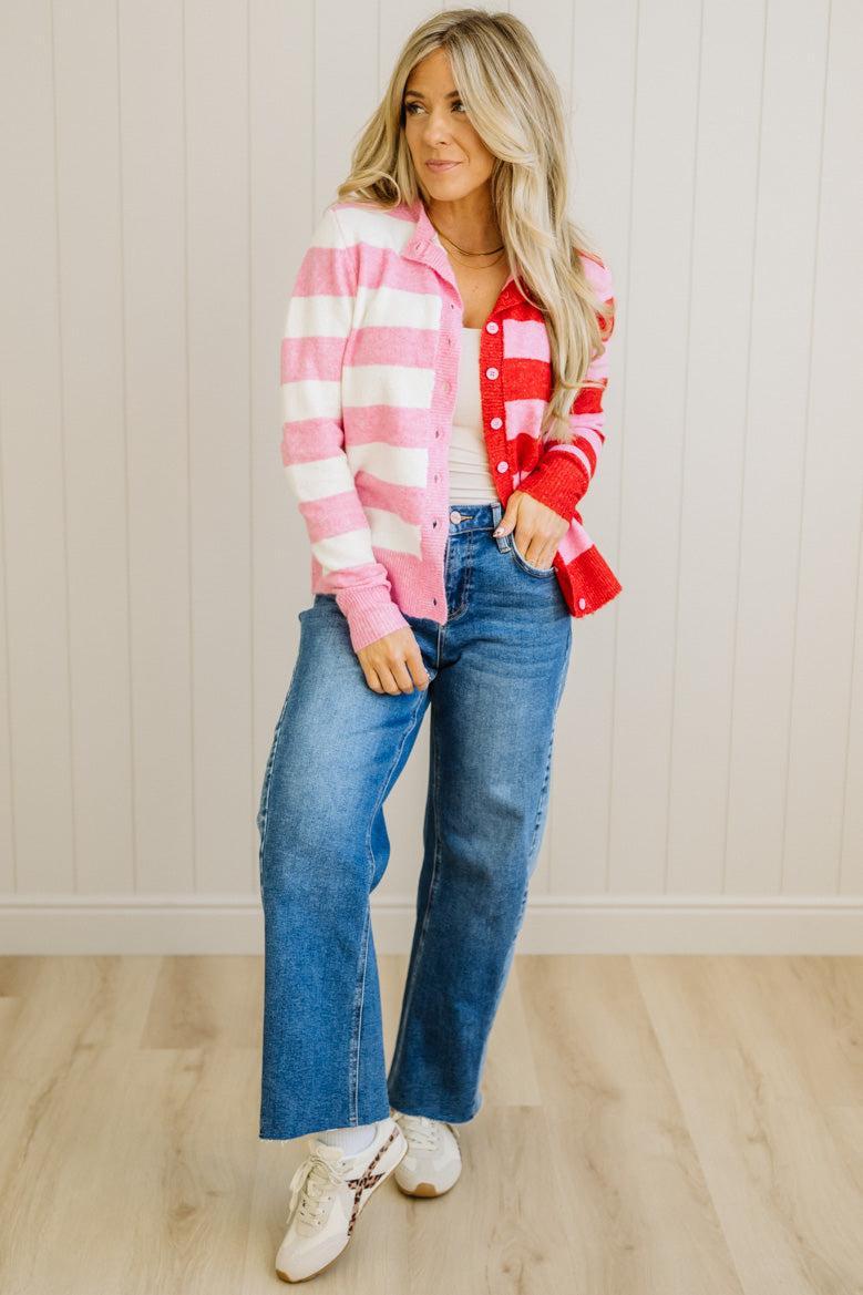Woman wearing a red and pink plaid shirt with blue jeans against a white paneled wall.