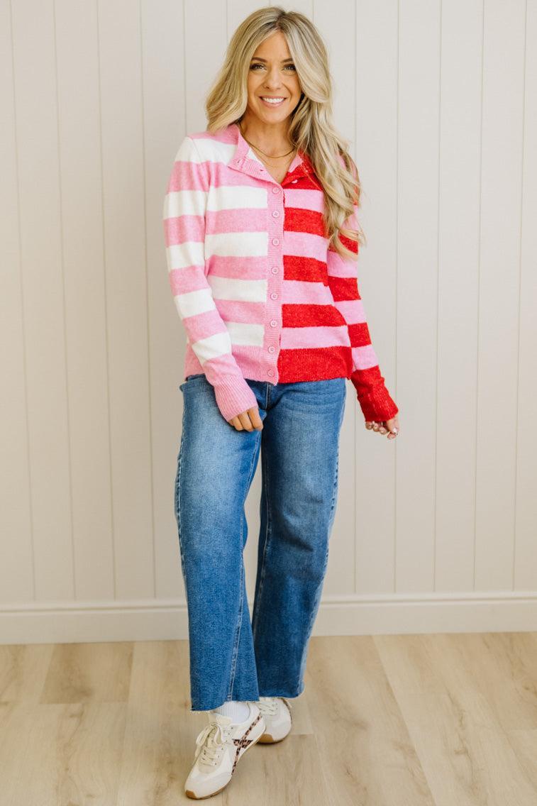 Woman wearing a pink and red striped sweater with blue jeans against a white paneled wall.