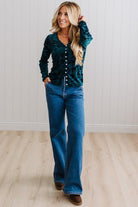 BLONDE WOMAN IN DARK JEANS WEARING A ROMANTIC VELVET BURNOUT TOP WITH FEATURES LIKE, BURNOUT VELVET MESH FABRICATION, SCALLOPED LACE EDGE ACCENTS, FUNCTIONAL BUTTONS AND LONG SLEEVES