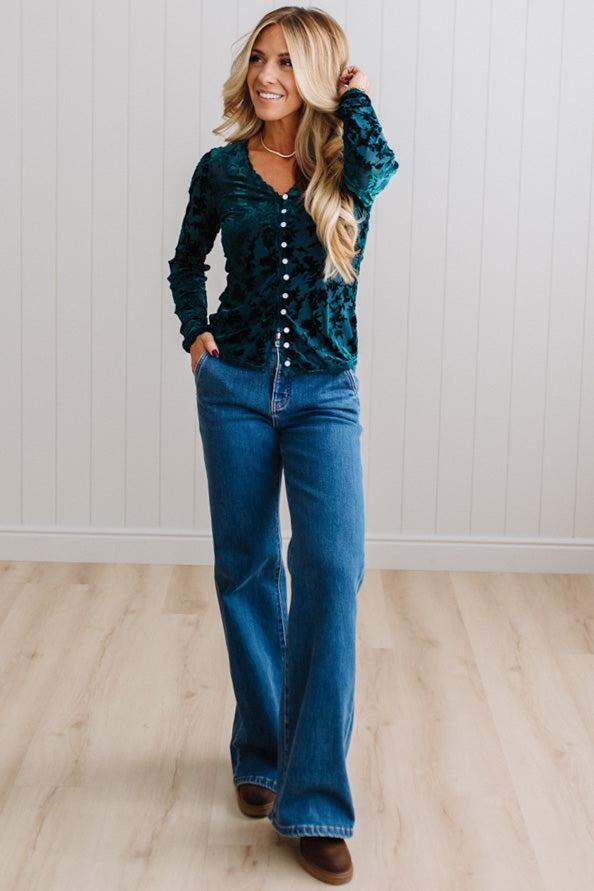 BLONDE WOMAN IN DARK JEANS WEARING A ROMANTIC VELVET BURNOUT TOP WITH FEATURES LIKE, BURNOUT VELVET MESH FABRICATION, SCALLOPED LACE EDGE ACCENTS, FUNCTIONAL BUTTONS AND LONG SLEEVES