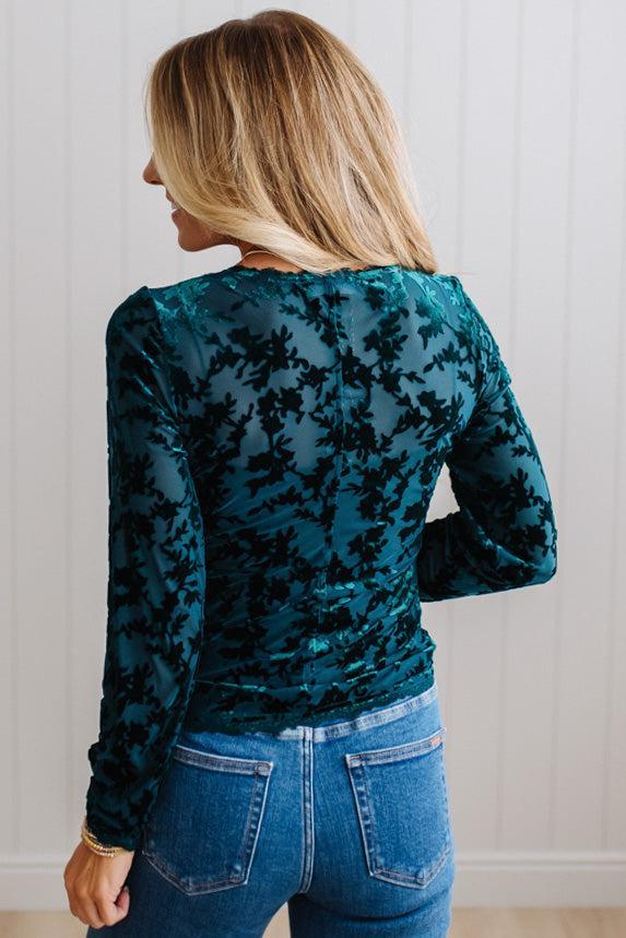 BLONDE WOMAN IN DARK JEANS WEARING A ROMANTIC VELVET BURNOUT TOP WITH FEATURES LIKE, BURNOUT VELVET MESH FABRICATION, SCALLOPED LACE EDGE ACCENTS, FUNCTIONAL BUTTONS AND LONG SLEEVES