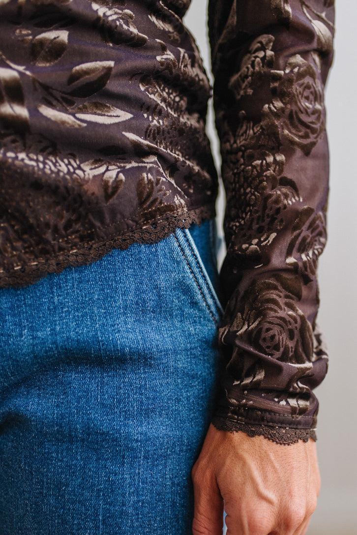 BLONDE WOMAN IN DARK JEANS WEARING A ROMANTIC VELVET BURNOUT TOP WITH FEATURES LIKE, BURNOUT VELVET MESH FABRICATION, SCALLOPED LACE EDGE ACCENTS, FUNCTIONAL BUTTONS AND LONG SLEEVES