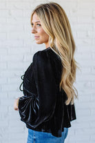 Woman wearing a black velvet top with lace-up details against a white brick wall.