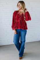 Woman wearing a red blouse and blue jeans against a white brick wall.