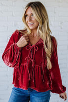 Woman wearing a red velvet top with blue jeans against a white brick wall.