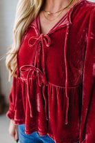 Red velvet top with lace-up front worn by a person, blurred background