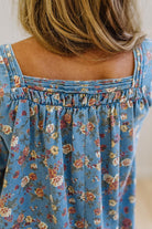 Close-up back view of a person wearing a blue floral top with a smocked neckline and thin straps.