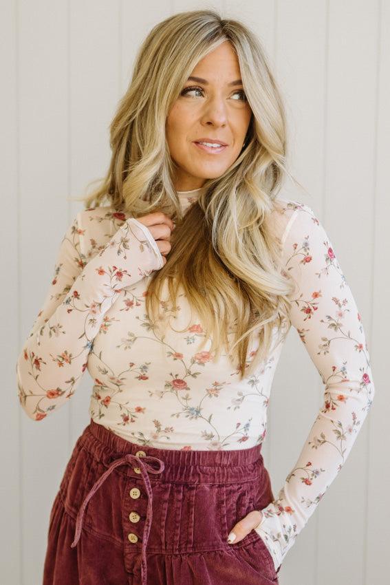 Woman wearing a floral blouse and burgundy skirt against a light background