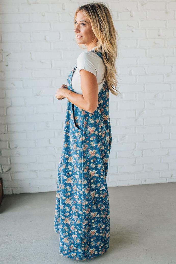 Woman wearing blue floral overalls against a white brick wall.