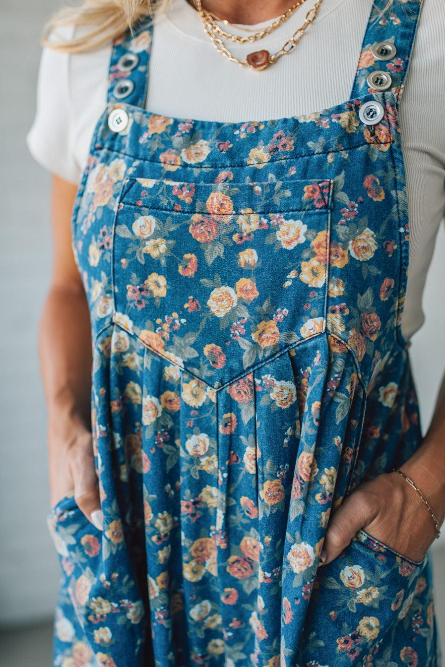 Person wearing blue floral overalls with a white background