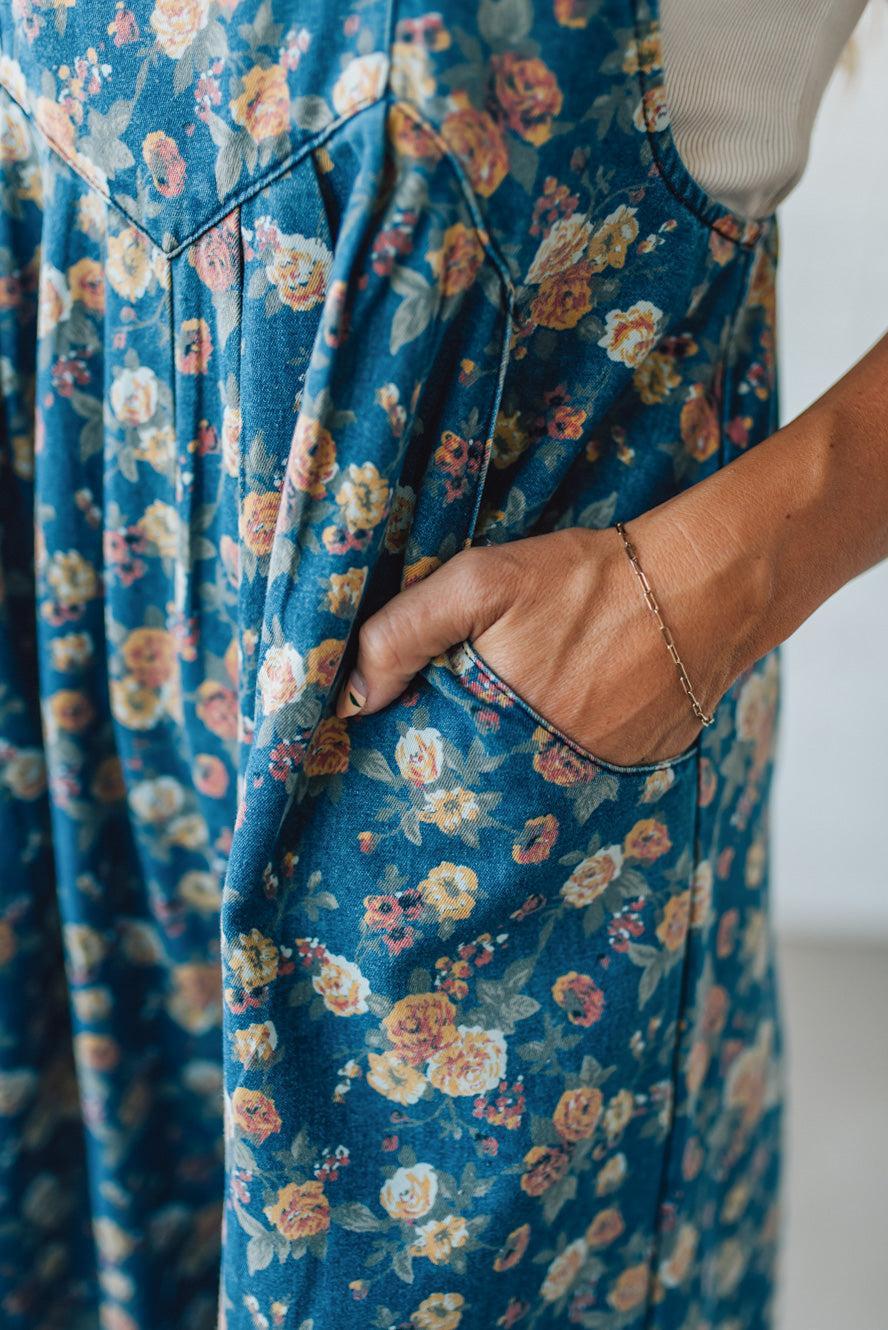 Close-up of a person wearing a blue floral overalls with a hand in the pocket.