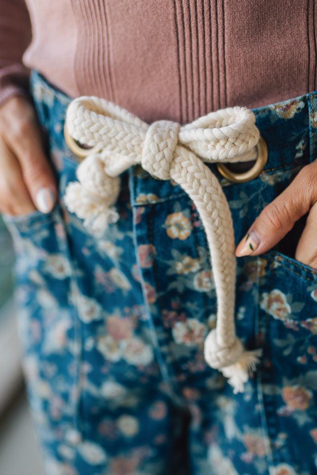 Close-up of a person wearing a brown top and blue floral pants with a decorative rope belt.