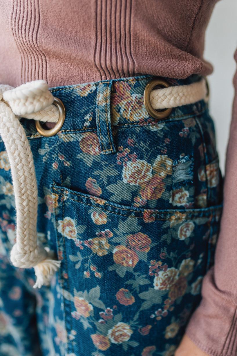 Person wearing a brown ribbed sweater and blue floral pants with a beige belt.