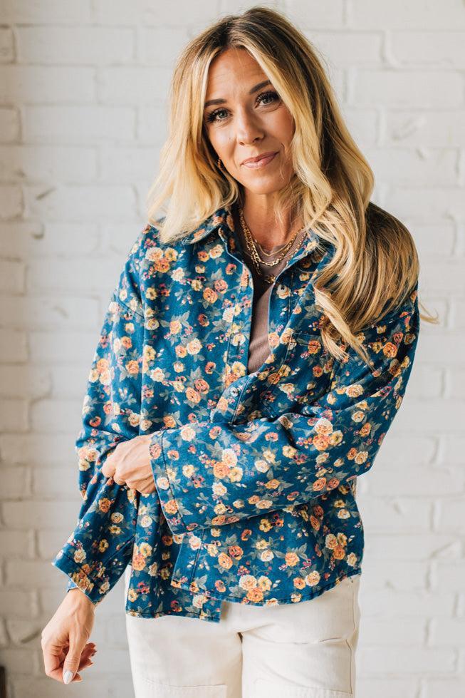 Woman wearing a blue floral jacket against a white brick wall