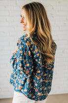 Woman wearing a blue floral blouse against a white brick wall.