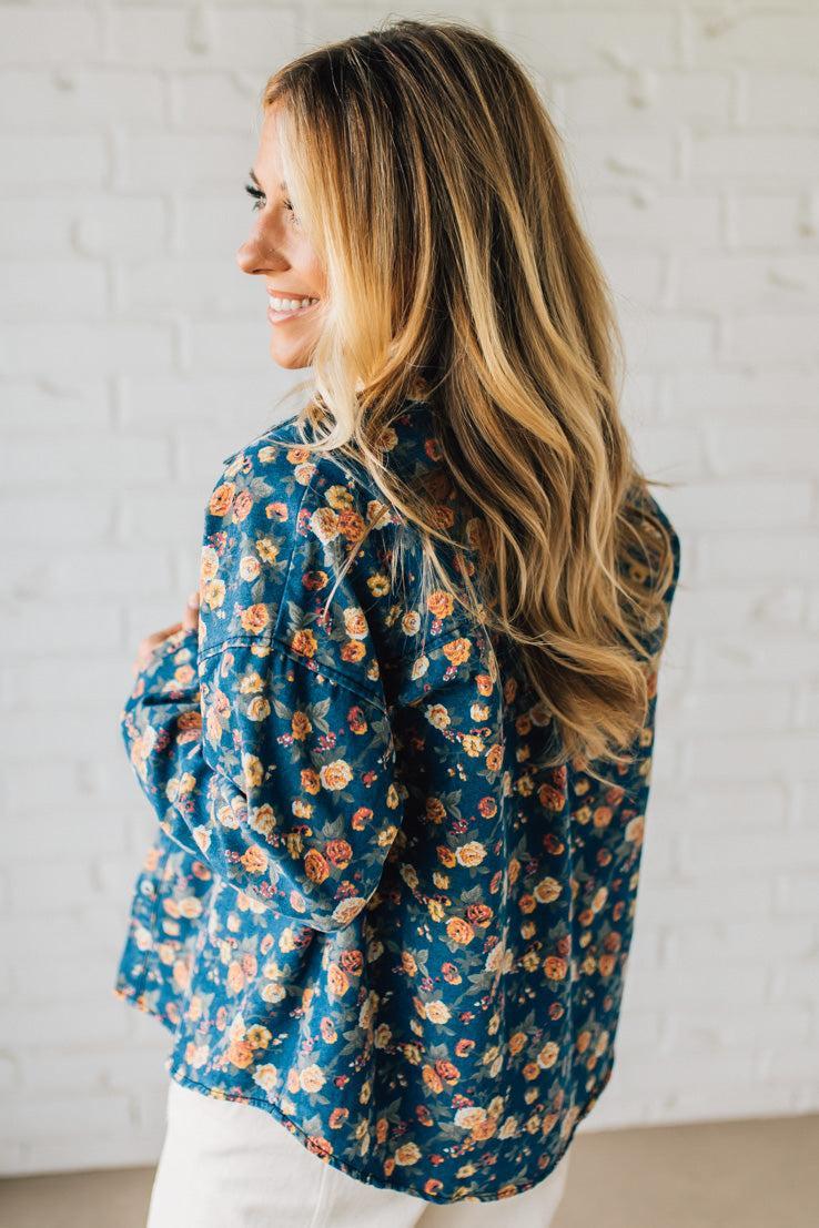Woman wearing a blue floral blouse against a white brick wall.