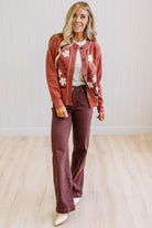 A woman modeling a rust-colored floral cardigan and matching brown wide-leg pants against a white paneled wall and light wood floor.