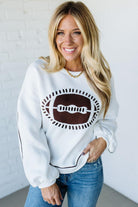 Woman wearing a white sweatshirt with a graphic design, standing against a plain background