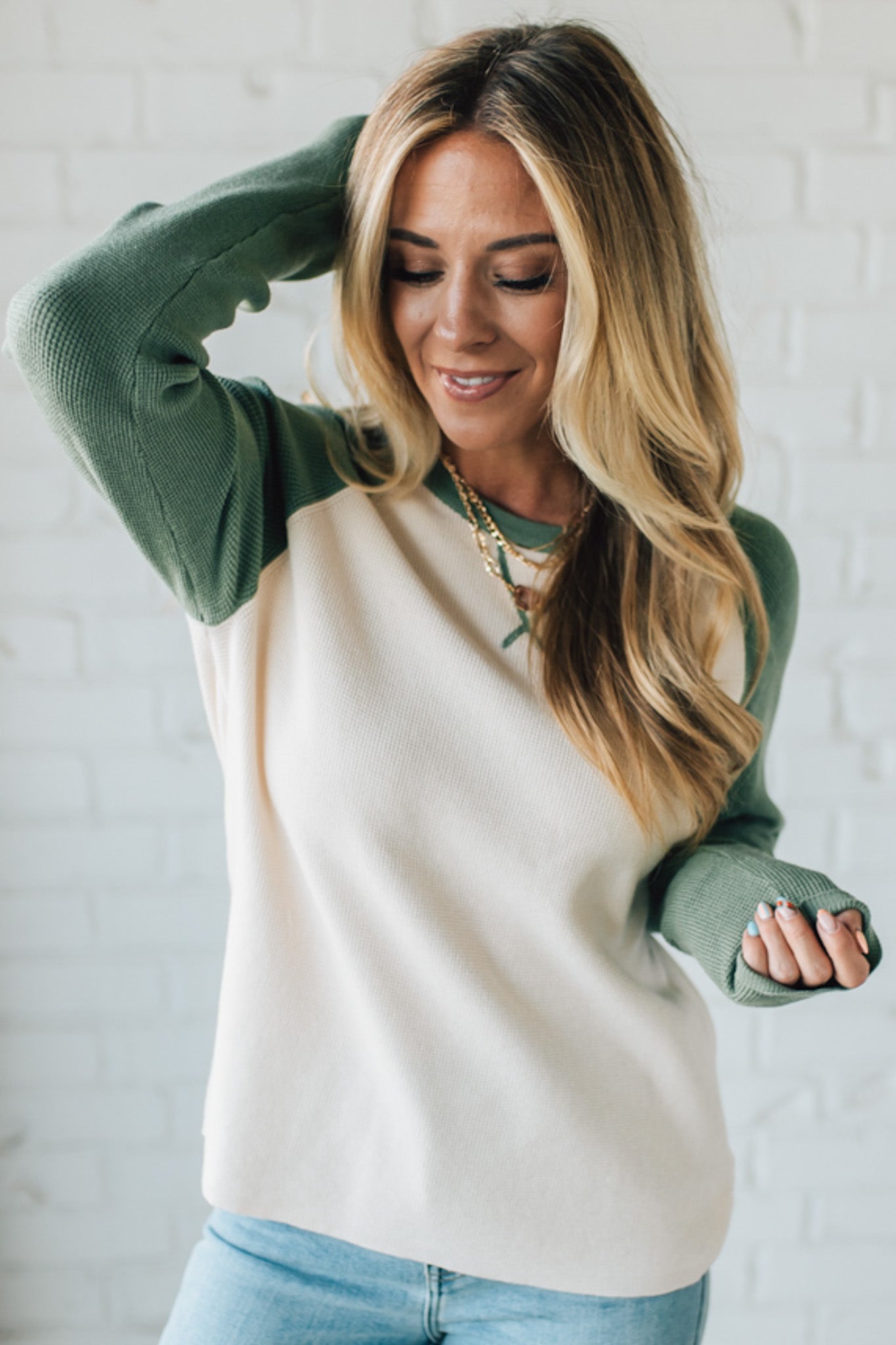 Woman wearing a green and cream sweater against a white brick wall.