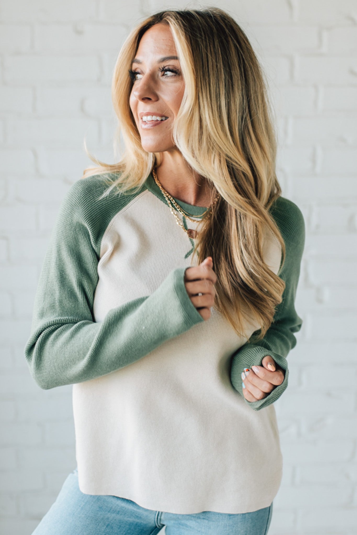 Woman wearing a green and white sweater against a white brick wall.