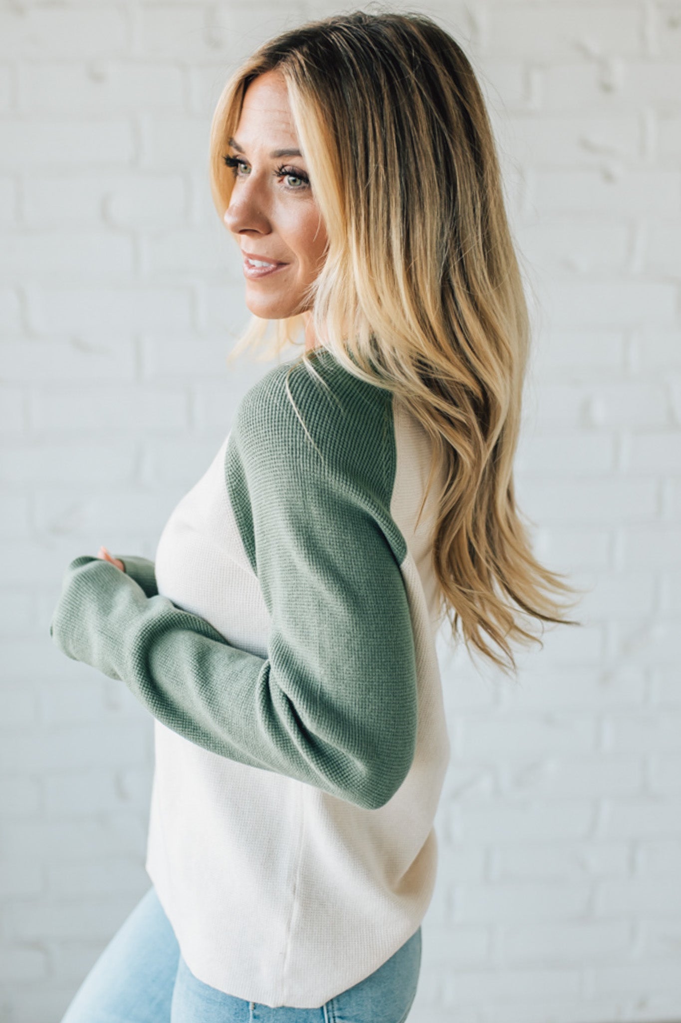 Woman wearing a green sweater over a white shirt with a white brick wall background