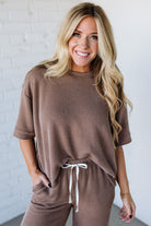 Woman wearing a brown ribbed lounge set against a white brick wall.