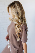 Woman with long, wavy blonde hair wearing a brown ribbed sweater against a white background