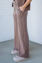 Person wearing brown ribbed pants and white sneakers against a white brick wall.