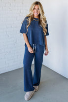 Woman wearing a blue waffle knit outfit against a white brick wall.