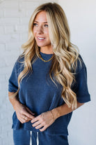 Woman wearing a blue ribbed sweater and pants against a white brick wall.